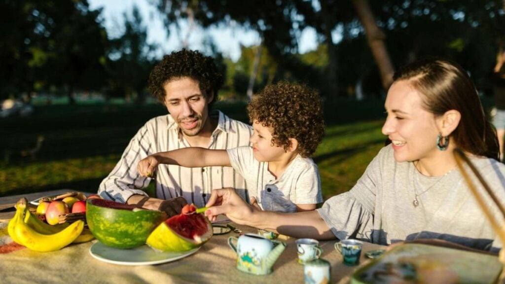 8208772 Happy family having a joyful picnic with fruits and snacks in a park during summer.