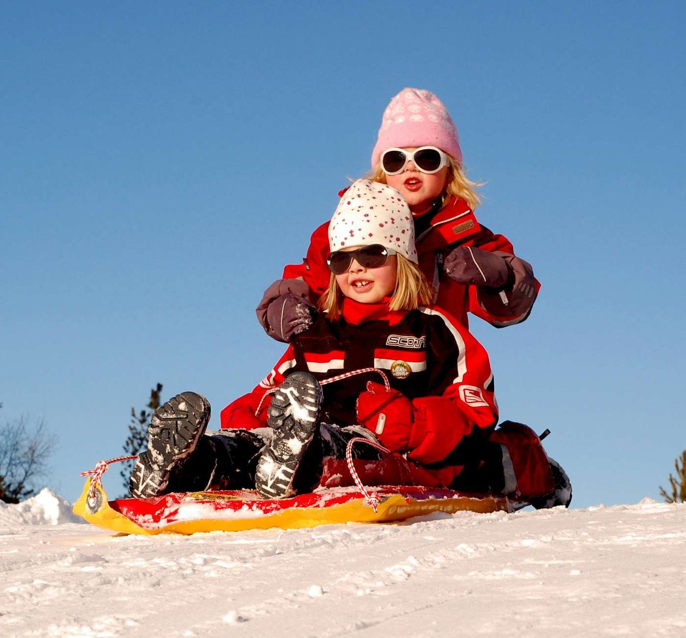 70448 Two children enjoying a fun sled ride down a snowy hill on a sunny winter day.
